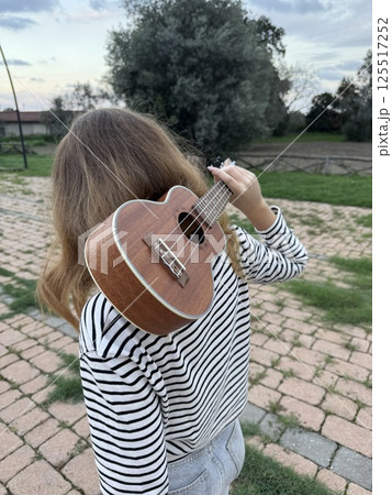Girl Makes Bow After Playing Ukulele Instrument In A Park 125517252