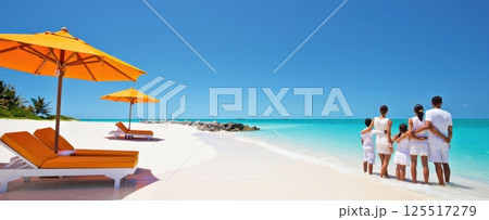 A joyful family enjoys time together on a pristine beach under clear blue skies. Bright orange umbrellas provide shade as they cherish moments by the shimmering water. 125517279