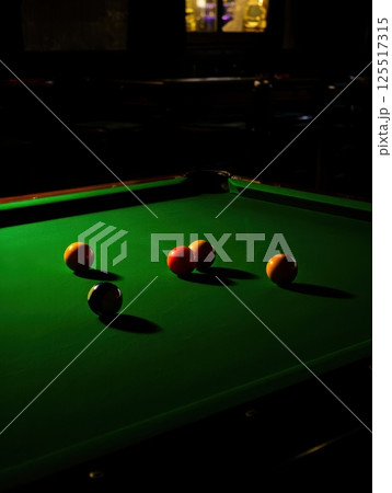 Five colorful balls lie on a vibrant green felt table surrounded by soft lighting in a cozy room setting the stage for an engaging game of skill and strategy among friends. 125517315