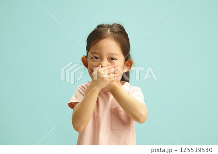 Ooops, i said it. Naughty korean Child Girl with Hand Over Mouth, does not want to tell the truth, tries to deceive or keep silent about something standing over blue isolated background. 125519530