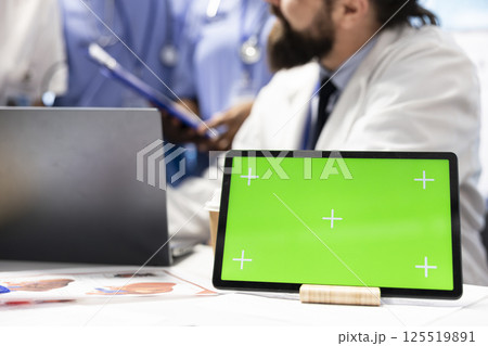 Doctors and nurses review radiography scans with a green screen on desk, discussing potential diagnosis and treatment plans in private clinic. Professional experts staff work with expertise. 125519891