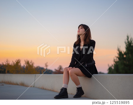 夕焼けの歩道で座って空を見上げる女性 125519895