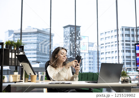 Female CEO taking a break from work and answering text messages on her smartphone, discussing with partners or friends in her high end business office. Social media updates online. Female CEO taking a break from work and answering text messages on her smartphone, discussing with partners or friends in her high end business office. Social media updates online. 125519902