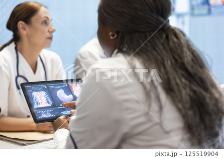 Medical professionals in a meeting examining organs on ct scan results. Skilled physicians and radiologists review x rays and hospital records to develop effective treatment plans. Collective work. 125519904