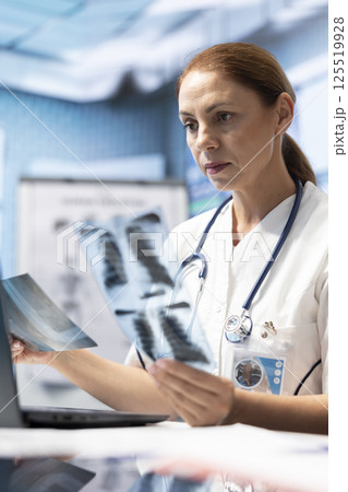 General practitioner examining x ray scans test results to find the right treatment in private clinic, medical specialist looking at radiography for a diagnostic. Woman physician working at facility. 125519928