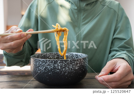 Cropped shot view of woman using chopsticks for eat Udon. Udon is a thick, white, ribbon-like noodle popular in Japanese cuisine. 125520647