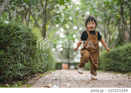 happy toddler girl running on pathway in garden 125521284