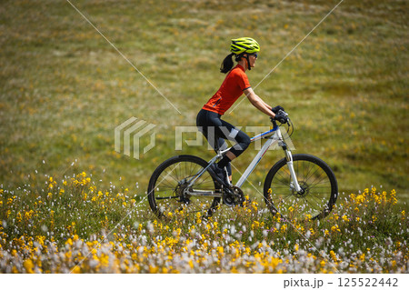 Woman riding mountain bike on beautiful flowering grassland mountain top Woman riding mountain bike on beautiful flowering grassland mountain top 125522442