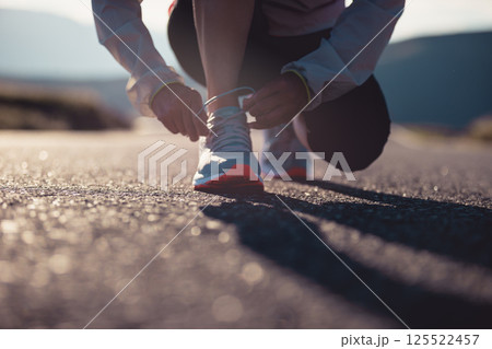 Woman runner tying shoelace on sunset mountain road 125522457