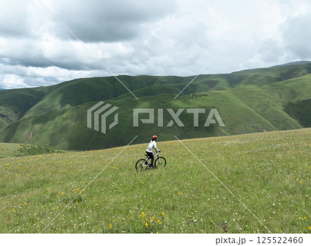 Aerial view of woman riding mountain bike on flowering grassland mountain trail 125522460