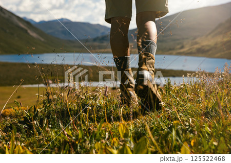 Hiker legs wearing leather boots hiking on high altitude mountain top,with a lake in the distance 125522468