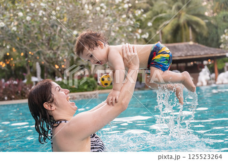 Caucasian woman holds son while swimming in pool on vacation. Caucasian woman holds son while swimming in pool on vacation. 125523264