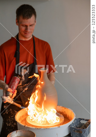 A potter burns a jug with a gas burner on a potter's wheel. Vertical photo.  125523333
