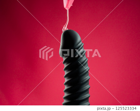 Lube pouring on black dildo on pink background. Lube pouring on black dildo on pink background. 125523334