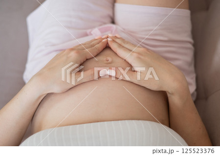 Pregnant woman holds her hands in a heart shape on her belly. Pregnant woman holds her hands in a heart shape on her belly. 125523376