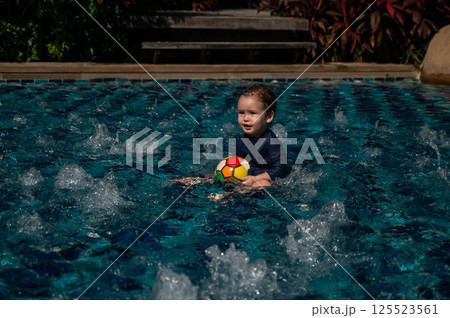 Caucasian one year old boy playing ball in swimming pool. Caucasian one year old boy playing ball in swimming pool. 125523561