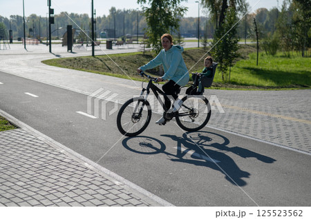 Caucasian woman riding a bicycle with her toddler son sitting behind her in a child seat.  125523562