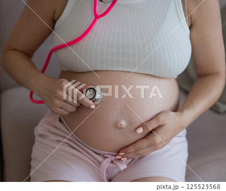 A pregnant woman listens to her baby's pulse using a phonendoscope. A pregnant woman listens to her baby's pulse using a phonendoscope. 125523568