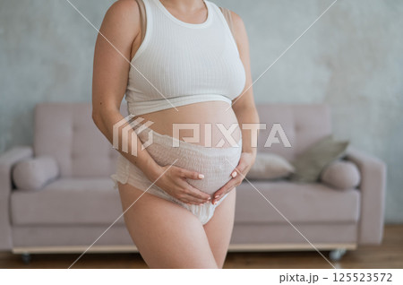 Caucasian pregnant woman in adult diapers suffers from incontinence. Close-up of belly. Caucasian pregnant woman in adult diapers suffers from incontinence. Close-up of belly. 125523572