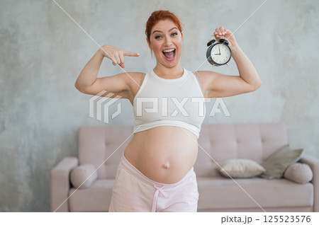 Caucasian pregnant woman holding alarm clock waiting for delivery.  125523576