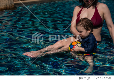 A Caucasian woman and her one-year-old son swim in a pool. A Caucasian woman and her one-year-old son swim in a pool. 125523696