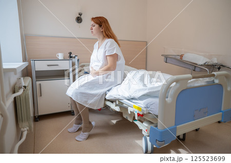 An unhappy woman sits on a couch and holds her stomach in a hospital room after giving birth. An unhappy woman sits on a couch and holds her stomach in a hospital room after giving birth. 125523699