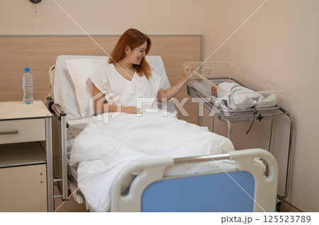 A young mother admires her newborn son in the maternity hospital.  125523789