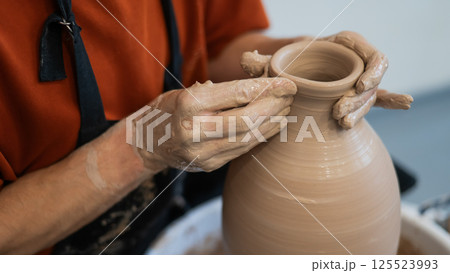 Close-up of a potter's hands making a ceramic vase on a potter's wheel. Close-up of a potter's hands making a ceramic vase on a potter's wheel. 125523993
