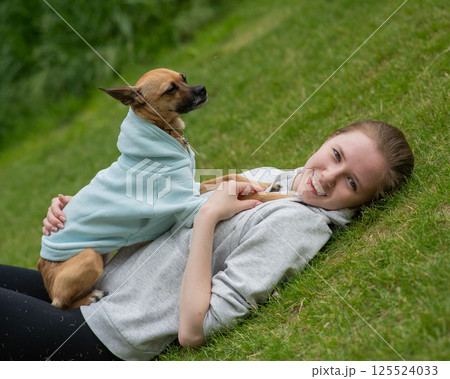 Young Caucasian woman lying on the lawn while walking with a small dog. Young Caucasian woman lying on the lawn while walking with a small dog. 125524033