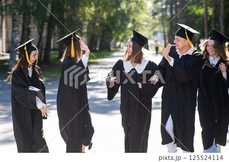 Row of happy young people in graduation gowns outdoors. Students are walking in the park. Row of happy young people in graduation gowns outdoors. Students are walking in the park. 125524114
