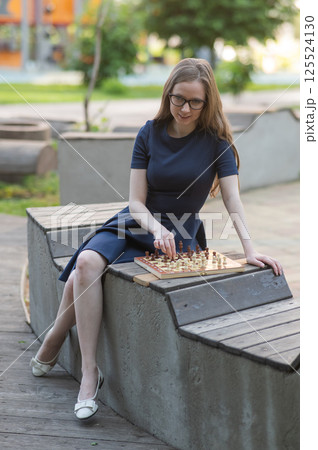 Caucasian woman playing chess outdoors. Caucasian woman playing chess outdoors. 125524130