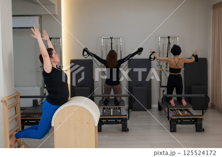 Three women doing Pilates on a reformer and a Pilates barrel.  Three women doing Pilates on a reformer and a Pilates barrel.  125524172