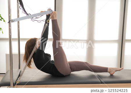 Woman doing Pilates on reformer. Woman doing Pilates on reformer. 125524225