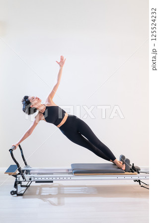 Asian woman doing pilates on reformer. Asian woman doing pilates on reformer. 125524232
