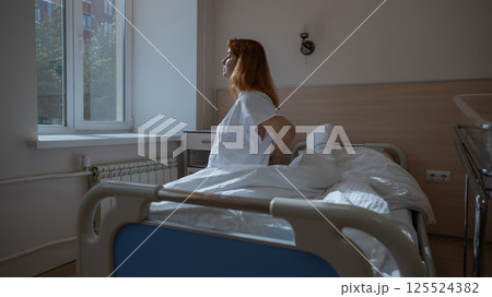 An unhappy woman sits on a couch and holds her stomach in a hospital room after giving birth. An unhappy woman sits on a couch and holds her stomach in a hospital room after giving birth. 125524382
