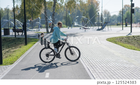 Caucasian woman riding bicycle with toddler son sitting behind her in child seat in park. Caucasian woman riding bicycle with toddler son sitting behind her in child seat in park. 125524383