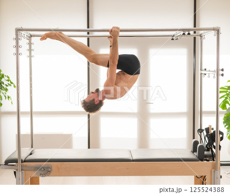 A man performs aerial exercises on a reformer machine. 125524388