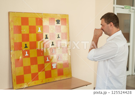 Caucasian man standing at wall mounted magnetic chessboard demonstration. Caucasian man standing at wall mounted magnetic chessboard demonstration. 125524428