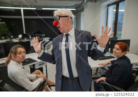 An elderly man in a clown costume fools around at work. 125524522