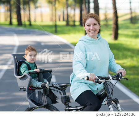 Caucasian woman riding a bicycle with her toddler son sitting behind her in a child seat. Caucasian woman riding a bicycle with her toddler son sitting behind her in a child seat. 125524530