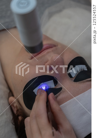 A woman undergoing eyelash extension procedure using an ultraviolet lamp. 125524557