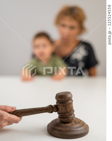 A judge hits a gavel against the backdrop of an elderly woman holding a child.  125524559