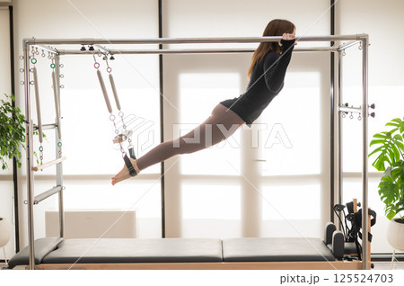 Caucasian woman doing aerial exercises on a reformer machine.  125524703