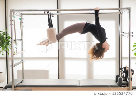 Caucasian woman doing aerial exercises on a reformer machine.  125524770