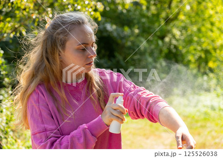 Woman spraying insect repellent at her hand outdoors during summer. Trying to kill mosquitoes and flies. Clearly visible spray droplets. Prevention disinfection against mosquito bite 125526038