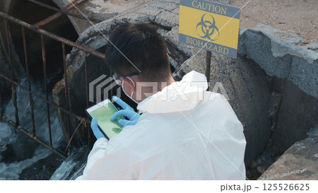 Ecologist sampling water of toxic chemicals from river touching screen on digital tablet, Biologist wear protective suit and mask collects sample of waste water from industrial, problem environment 125526625