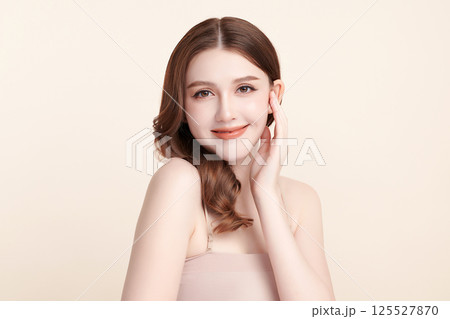 A beautiful young Asian woman with clean, fresh skin against a beige background. Skincare, facial treatment, cosmetology, beauty, and spa. An elegant portrait of an Asian woman. 125527870