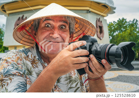funny elderly man travel photographer in Vietnamese hat takes pictures with camera at pagoda in Nha Trang in Vietnam. Tourism and travel in Asia 125528610