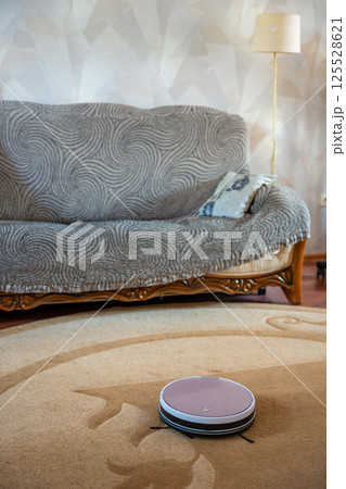 Robot vacuum autonomously cleaning a carpet at home. Concept of smart cleaning technology and automated home maintenance. Robot vacuum autonomously cleaning a carpet at home. Concept of smart cleaning technology and automated home maintenance. 125528621