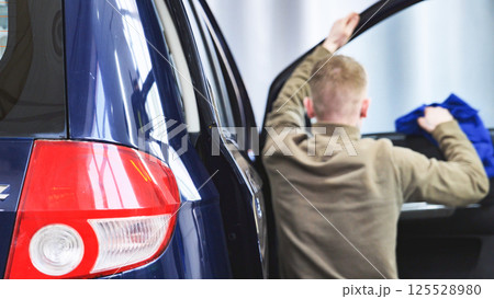 Car wash employee cleaning vehicle interior with microfiber cloth 125528980